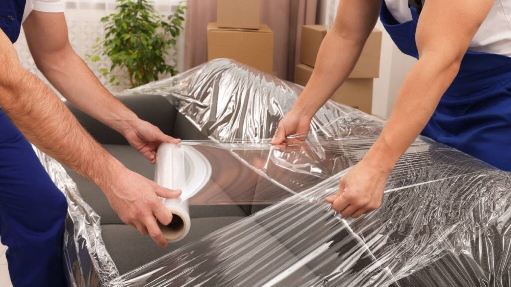 Professional movers packing a sofa with bubble wrap in a Dubai apartment